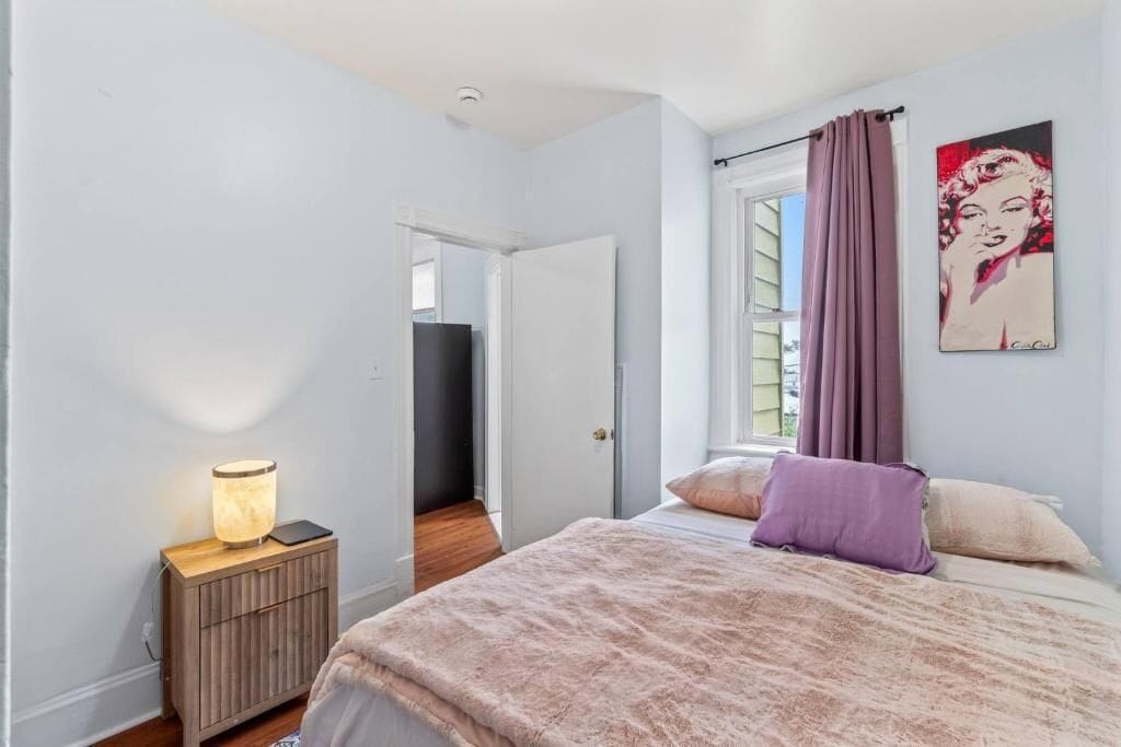 A bedroom with a bed, a bedside table with a lamp, a door, and a window with curtains.