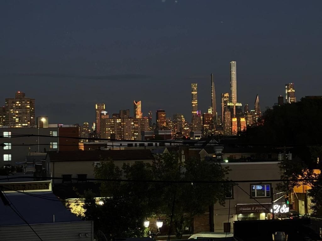 Horizonte urbano nocturno con edificios iluminados y una señal de calle visible.