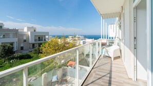 Un balcón con vistas al mar, una silla blanca y una barandilla de cristal.