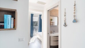 Un baño moderno con lavamanos, espejo y detalles decorativos. Se ve una estantería con libros en el pasillo.