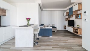 Una cocina moderna con una isla central, una zona de comedor con sofá y un televisor sobre una estantería de madera.