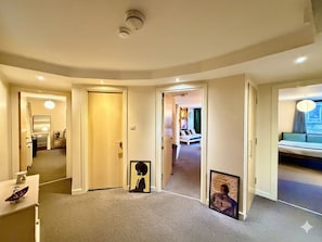 A hotel corridor with multiple doors leading to rooms, a bed in the background, and framed pictures on the walls. - Stylish 2BR City Centre Flat | 3 min to Central Station | Family Sized (Glasgow)