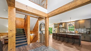 A spacious kitchen with wooden beams, a central island with bar stools, and a staircase leading to an upper level.