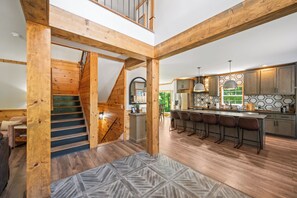 Eine geräumige Küche mit Holzbalken, einer zentralen Kochinsel mit Barhocker und einer Treppe, die in ein Obergeschoss führt.