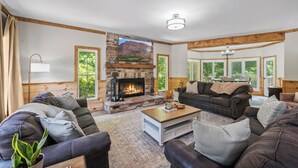 A cozy living room with a stone fireplace, comfortable seating, and large windows.