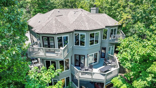 A multi-level house with balconies, large windows, and a surrounding lush green landscape.