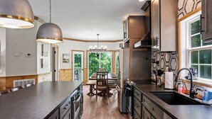A kitchen with a central island, wooden cabinetry, and a view of greenery outside.