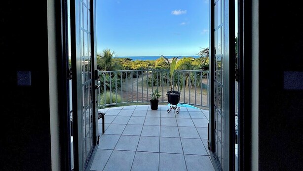 A balcony with a ceiling fan, potted plants, and a view of the ocean. - Vieques BioBay B&B, The Palm Room: Sleep Under the Stars, Paddle the Glowing Bay (Vieques)