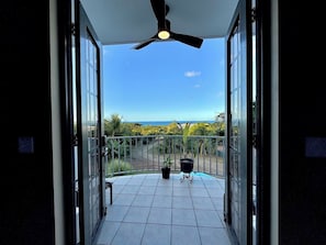 Un balcon doté d’un ventilateur de plafond, de plantes en pot et offrant une vue sur l’océan.