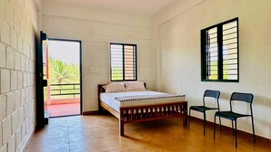 A bedroom with a bed, two chairs, a window, and a door leading to an outdoor area. - Nischala Stay at Isha Yoga Center (Coimbatore)