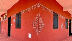 A red building with black doors and windows, a patterned design on the wall, and a flat roof. - Nischala Stay at Isha Yoga Center (Coimbatore)