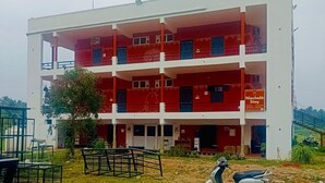 A multi-story building with balconies, a sign indicating 'Nishchala Stay,' and a gated entrance. - Nischala Stay at Isha Yoga Center (Coimbatore)