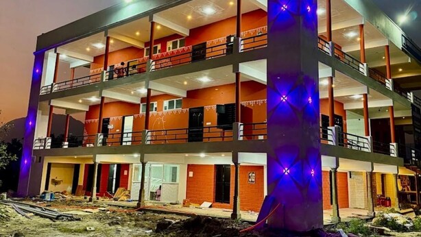 A multi-story building with balconies, a central column, and a construction site in front. - Nischala Stay at Isha Yoga Center (Coimbatore)