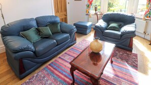 A living room with a blue sofa, a matching armchair, a glass coffee table, and a colorful rug.