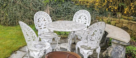 Un patio ajardinado con una mesa redonda y seis sillas, rodeado de muros de piedra y follaje.