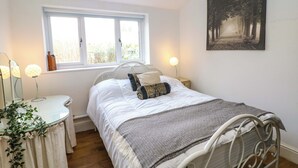A bedroom with a bed, bedside lamps, a window, a bedside table, a mirror, a plant, and a painting on the wall.