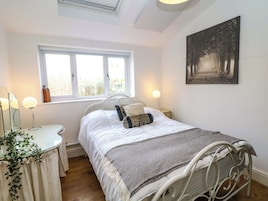 Un dormitorio con cama, lámparas de noche, ventana, mesita de noche, espejo, planta y un cuadro en la pared.
