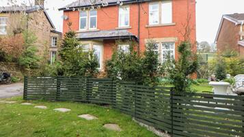 Ein Wohnhaus mit Ziegelverkleidung, einem Vorgarten mit trittfesten Steinen und einem grünen Zaun.