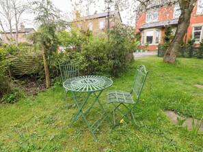 Una mesa y sillas de metal verde en un jardín con césped y arbustos.