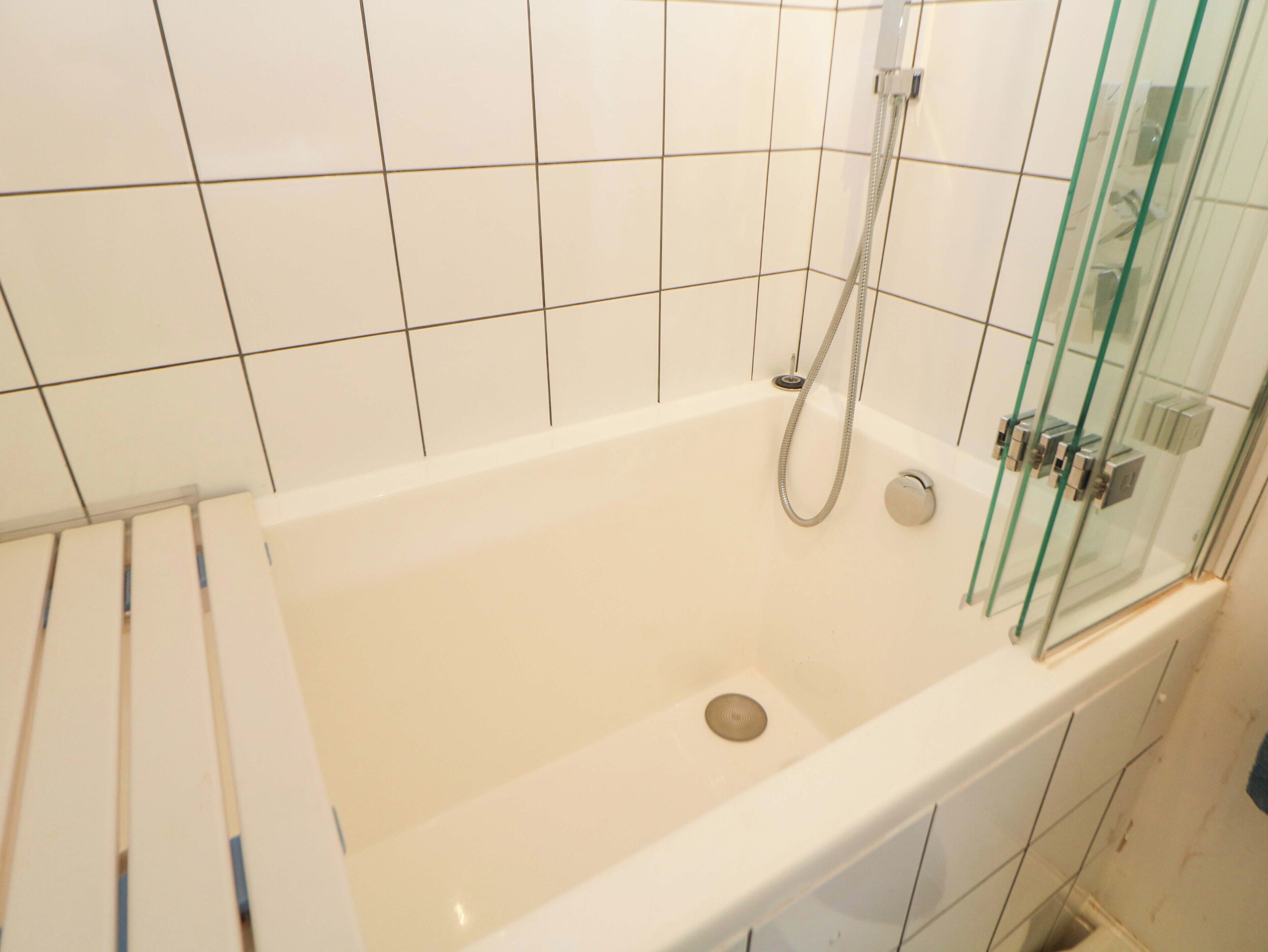 A bathroom with a bathtub, glass shower enclosure, and white tiled walls.