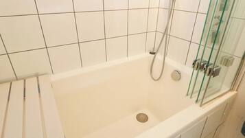 A bathroom with a bathtub, glass shower enclosure, and white tiled walls.