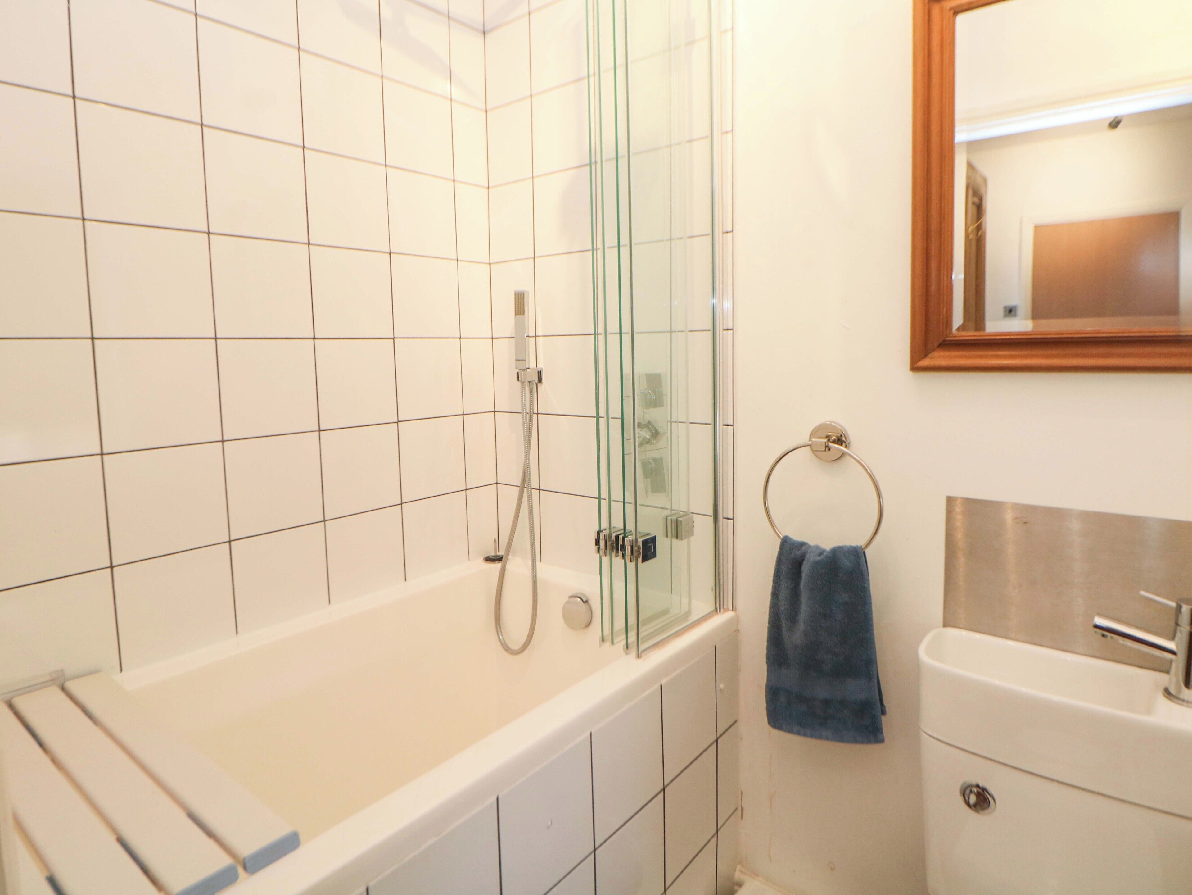 Um banheiro com chuveiro em cabine de vidro, banheira branca, porta-toalhas com uma toalha azul e pia com espelho acima.
