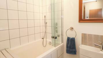 Um banheiro com chuveiro em cabine de vidro, banheira branca, porta-toalhas com uma toalha azul e pia com espelho acima.