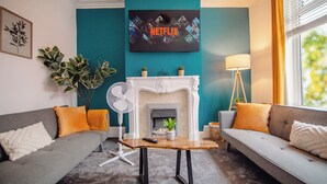 Ein Wohnzimmer mit Kamin, zwei Sofas, einem Couchtisch und einem an der Wand montierten Fernseher, der 'NETFLIX' zeigt.