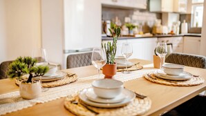 Ein Esszimmertisch ist gedeckt mit Tellern, Schüsseln und Besteck, mit einem Topf einer Pflanze und einer Blumenvase.