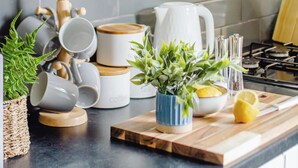Eine Küche mit weißen Schränken, einer gefliesten Spritzschutzwand, einem Holzschneidebrett, einem Blumentopf und verschiedenen Küchenutensilien.