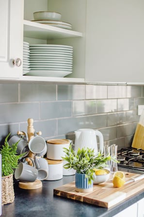 A kitchen with white cabinets, a tiled backsplash, a wooden cutting board, a potted plant, and various kitchenware. - Blue Lagoon Retreat Escape | Free Parking | 16PPL (Sheffield)