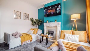 Ein modernes Wohnzimmer mit Kamin, zwei Betten, einem Fernseher und einer Pflanze.