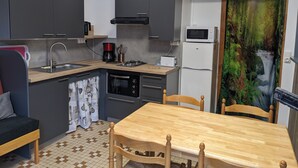 Cocina compacta con lavamanos, estufa, microondas y refrigerador. Hay una mesa de comedor con sillas y una ventana que da a un bosque.