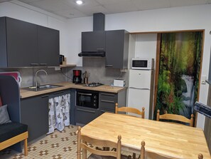 A compact kitchen with a sink, stove, microwave, and refrigerator. There is a dining table with chairs and a window with a view of a forest. - Family Villa - Les Cabris (La Bourboule)