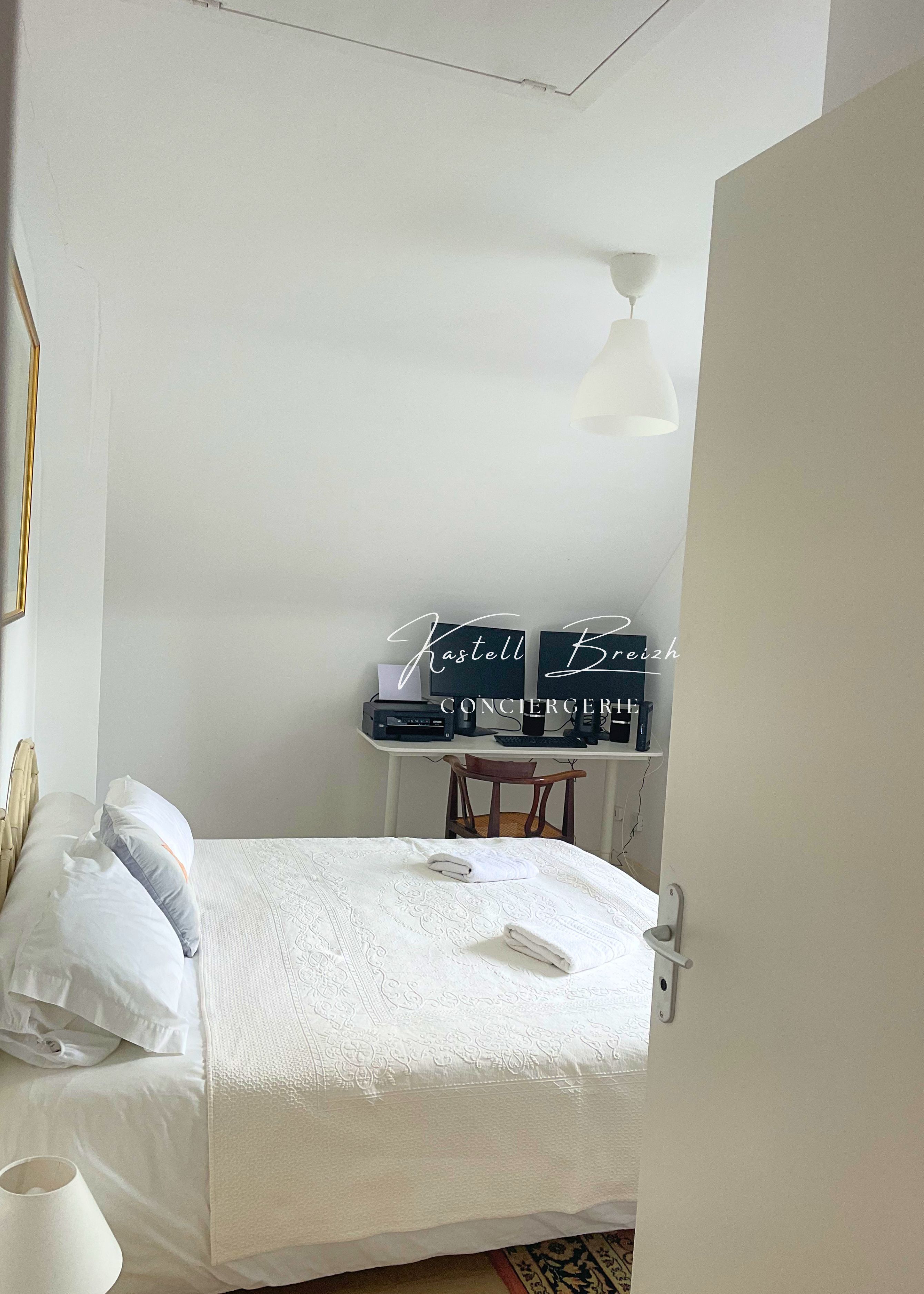 Un dormitorio con una cama bien hecha, un escritorio con una computadora y una lámpara colgante.