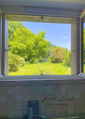 Ein Fenster mit Gartenblick, eine Wand mit Kacheln und einem Logo sowie ein Metall-Wasserhahn.