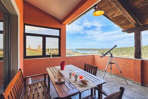 Un balcon avec une table en bois, des chaises, un télescope et une vue sur le paysage.