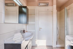Une salle de bain équipée d’un lavabo, d’un miroir, d’une serviette et d’une cabine de douche en verre.