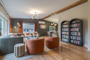 A modern living room with a sofa, ottomans, a coffee table, a bookshelf, and a dining area.