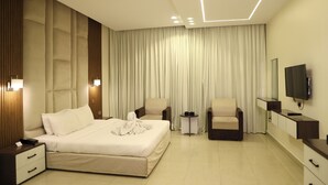 Ein modernes Hotelzimmer mit einem großen Bett, zwei Sesseln, einem Fernseher und einem kleinen Tisch.