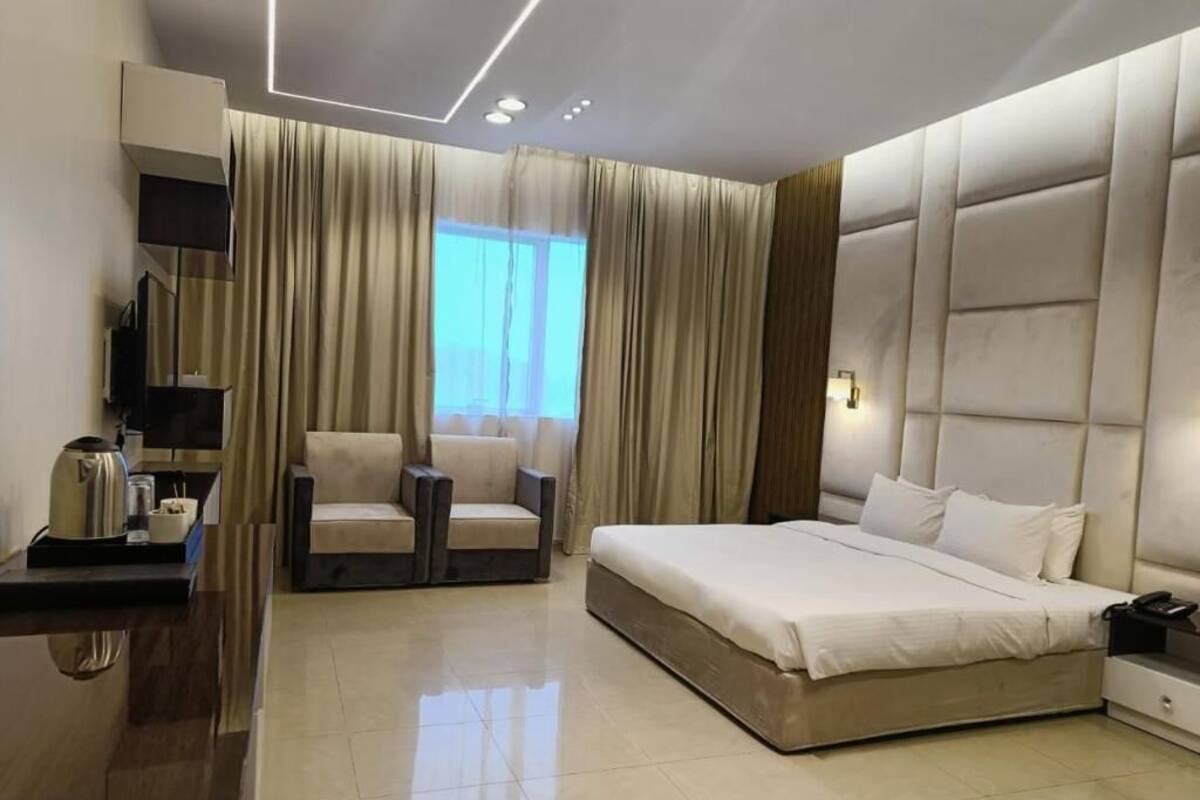 A modern hotel room with a large bed, a seating area, a flat-screen TV, and a window with curtains.