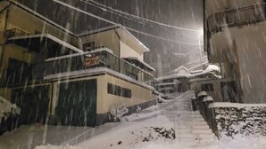 A snowy residential street with houses on either side, a staircase leading to a second floor, and a visible sign on the left house. - Charming mountain apartment: relaxation for couples, families and pets, bbq (Sasso)