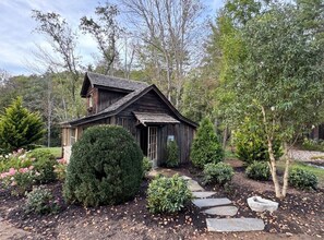 Un chalet rustique en bois, avec un chemin de pierres menant à l’entrée, entouré de divers arbustes et arbres.