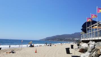 A beach with clear skies, a sandy shore, and a rocky outcrop.