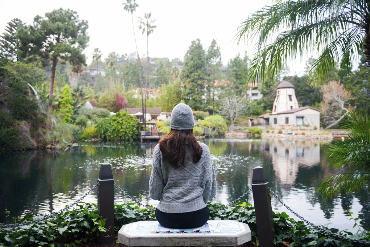 A person sitting by a calm body of water with a building in the background.