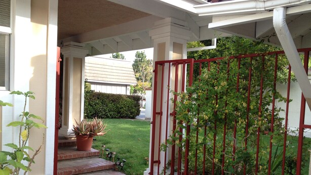 A covered porch with a red gate, potted plants, and a lawn.