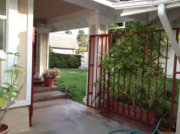 A covered porch with a red gate, potted plants, and a lawn.