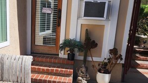 A front entrance with a wooden door, a welcome sign, a potted plant, and a small statue.