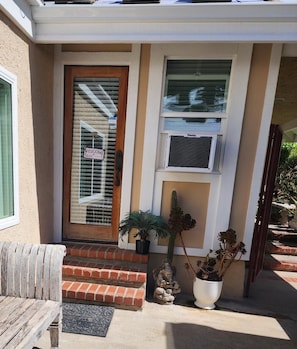 A front entrance with a wooden door, a welcome sign, a potted plant, and a small statue.