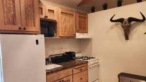 A kitchen with wooden cabinets, a white refrigerator, a gas stove, and a trash bin.
